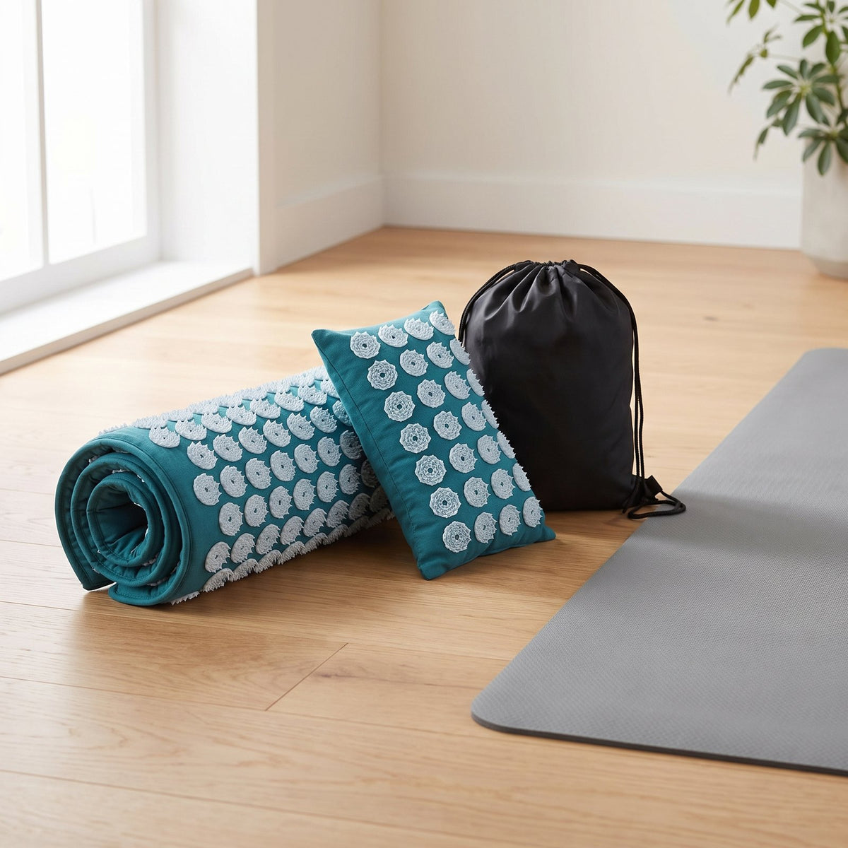 Rolled teal AcuRelief acupressure mat, neck pillow and black drawstring bag on a wooden floor