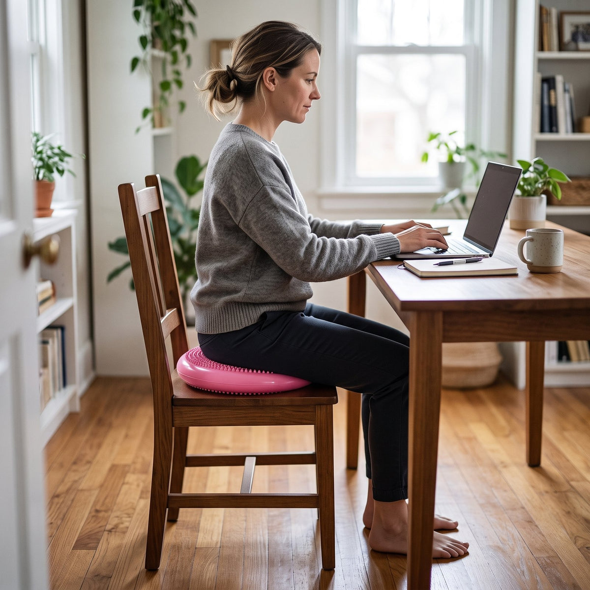 Woman sitting on the pink BalancePro wobble cushion on a four-legged wooden chair at her desk