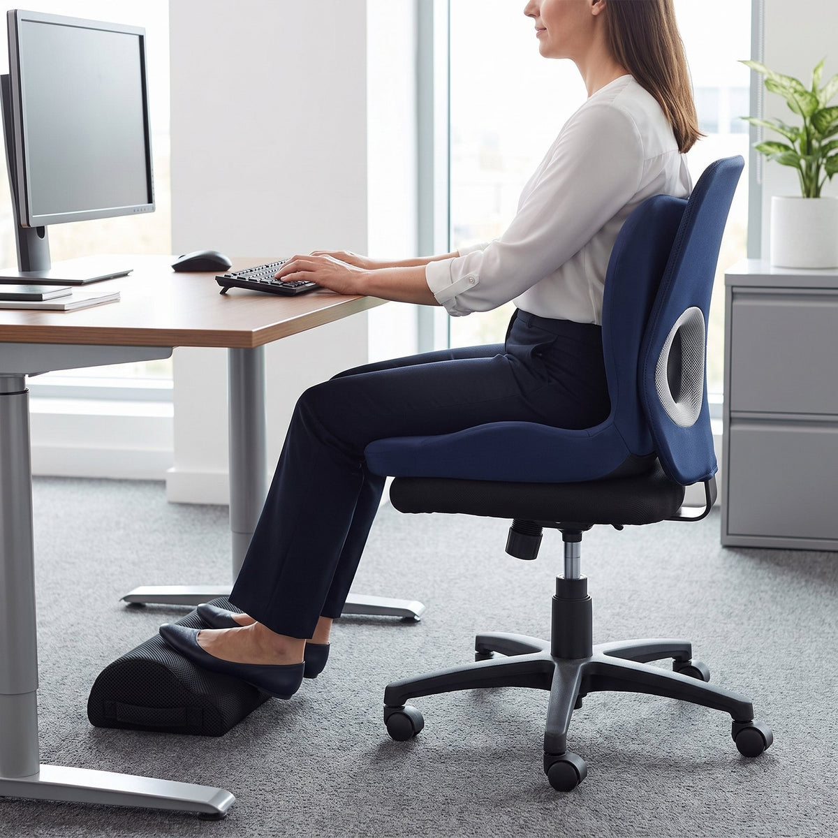 Woman seated on the navy cushion at her desk with her feet on the black mesh footrest