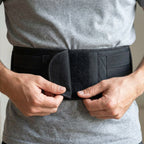 Hands fastening the hook-and-loop front flap of the black CoreGuard Pro back support belt