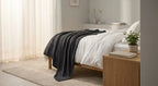 Dark gray GravityRest weighted blanket draped over a bed with white sheets