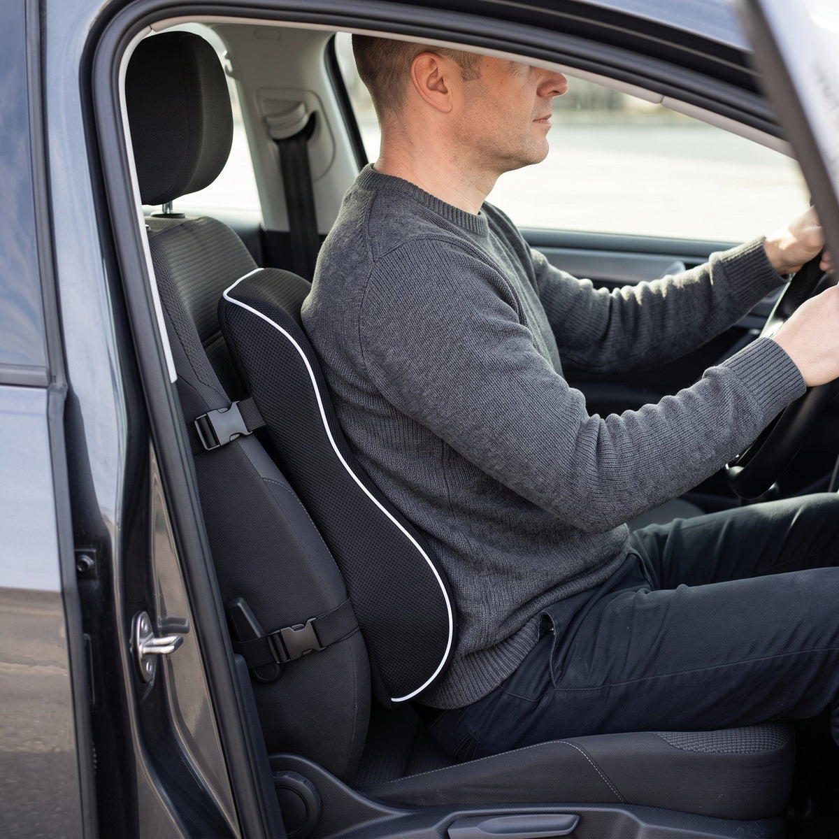 Driver seated with the black ErgoBack lumbar pillow strapped to a gray fabric car seat