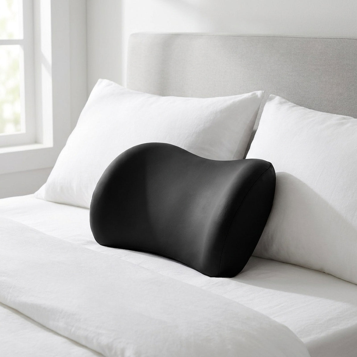 Black NightArc lumbar pillow on a bed with white bedding