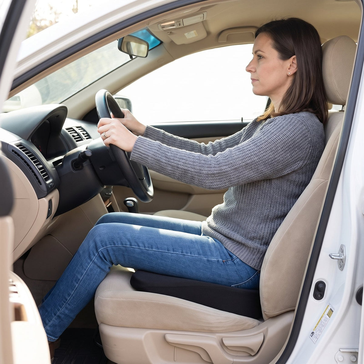 Petite woman driving, seated on a black RideRise booster cushion on the driver's seat