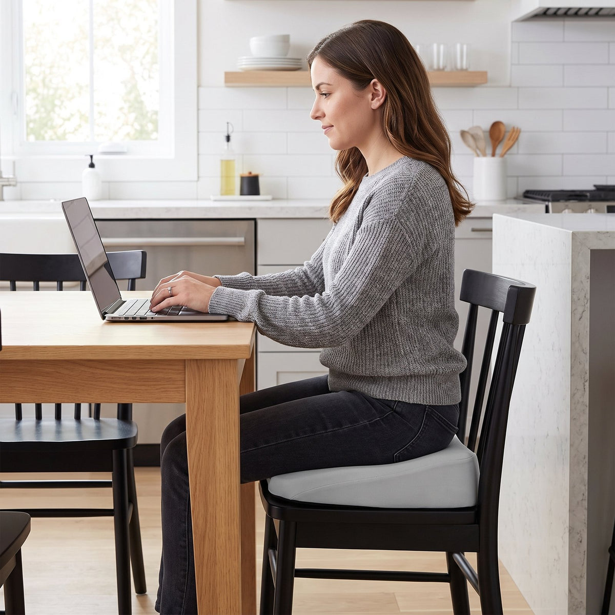 Woman working at a dining table, seated on a gray RideRise cushion on a wooden chair