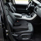 Black SciatiGuard U-cut seat cushion on the black leather driver's seat of an SUV, cutout against the backrest