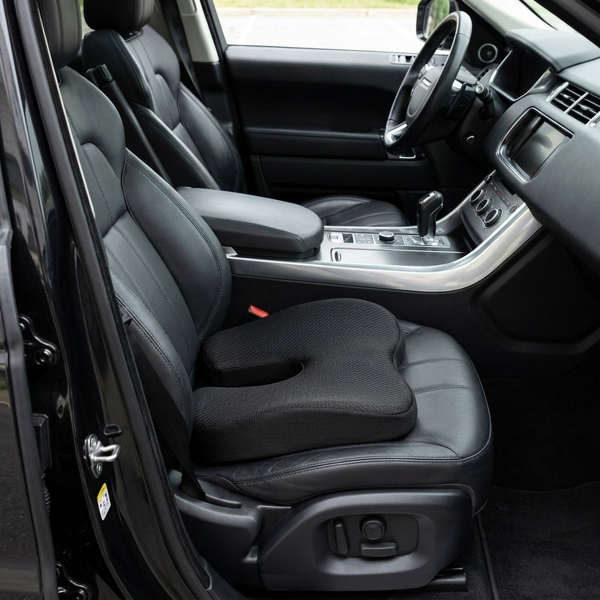 Black SciatiGuard U-cut seat cushion on the black leather driver's seat of an SUV, cutout against the backrest