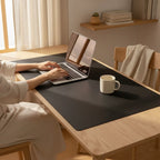Black desk mat under a laptop and mug on a wooden desk; laptop and mug not included