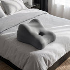 Gray LegLoft contoured leg rest pillow at the foot of a bed with light gray linen