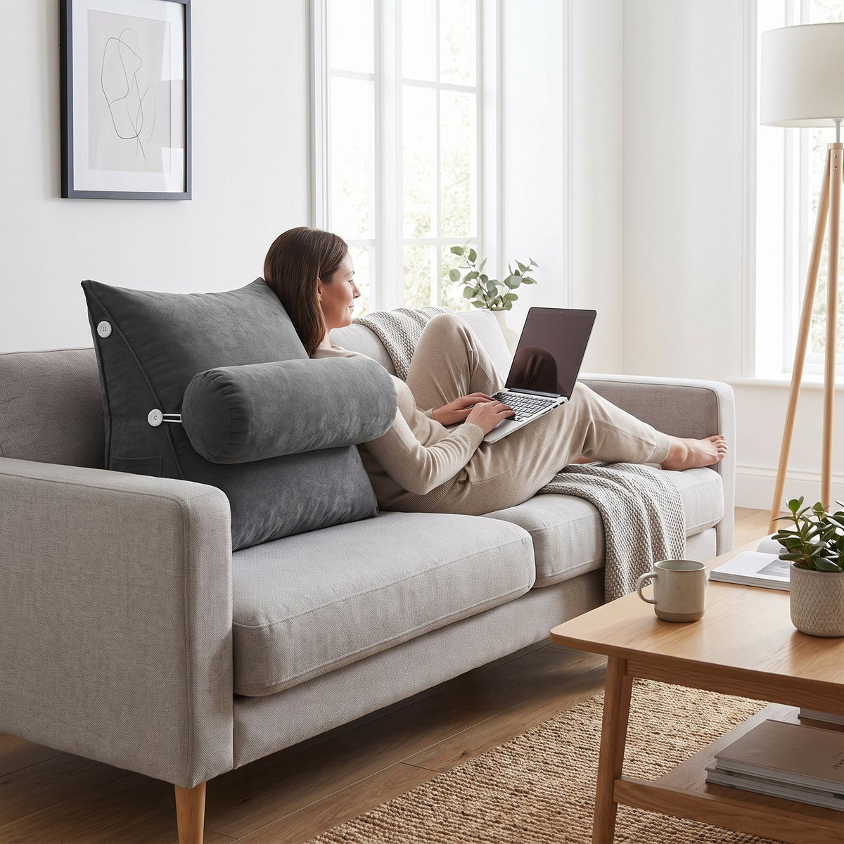 Woman with a laptop on a sofa, leaning on a gray WedgeRest backrest pillow